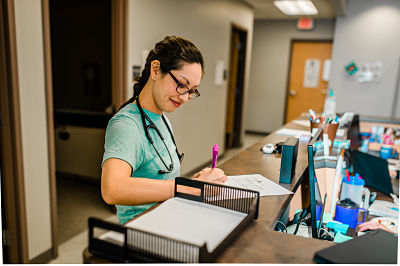 Picture of a female Nurse with a pen and piece of paper writing.
